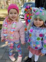 Grupa radosnych dzieci w kolorowych, wiosennych strojach maszeruje ulicami miasta, niosąc kwiaty i dekoracje, świętując pierwszy dzień wiosny