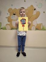 Dziecko trzyma w rękach kolorową pracę plastyczną przedstawiającą jego wymarzony lizak, z uśmiechem prezentując ją na konkurs 
