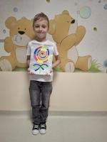 Dziecko trzyma w rękach kolorową pracę plastyczną przedstawiającą jego wymarzony lizak, z uśmiechem prezentując ją na konkurs 