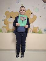 Dziecko trzyma w rękach kolorową pracę plastyczną przedstawiającą jego wymarzony lizak, z uśmiechem prezentując ją na konkurs 