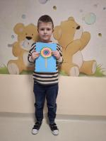 Dziecko trzyma w rękach kolorową pracę plastyczną przedstawiającą jego wymarzony lizak, z uśmiechem prezentując ją na konkurs 