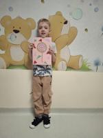 Dziecko trzyma w rękach kolorową pracę plastyczną przedstawiającą jego wymarzony lizak, z uśmiechem prezentując ją na konkurs 