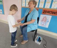 Dzieci z grupy „Malinki” słuchają z zaciekawieniem opowieści pani pielęgniarki. Dzieci oglądają przybory medyczne podczas zajęć o zdrowiu.