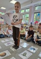 Dzieci biorące udział w zajęciach o kosmosie – oglądają ilustracje planet, bawią się w kosmiczną podróż i wykonują tematyczne zadania.